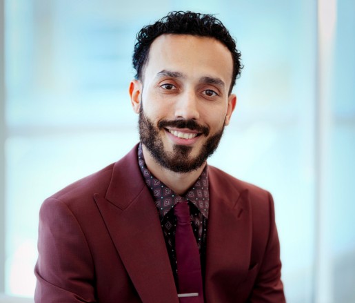 Luke Figueroa, a man with short curly hair, mustache, and beard, wearing a professional business suit