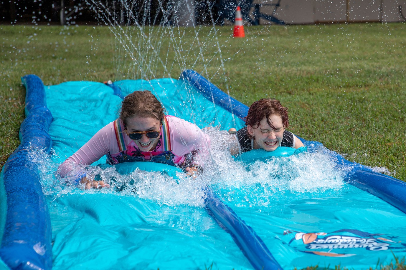 Two students slide along a waterslide sending up waves.