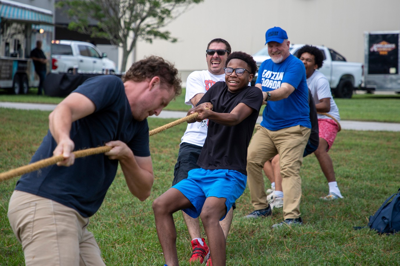 A group of diverse male students play tug-of-war on the lawn.