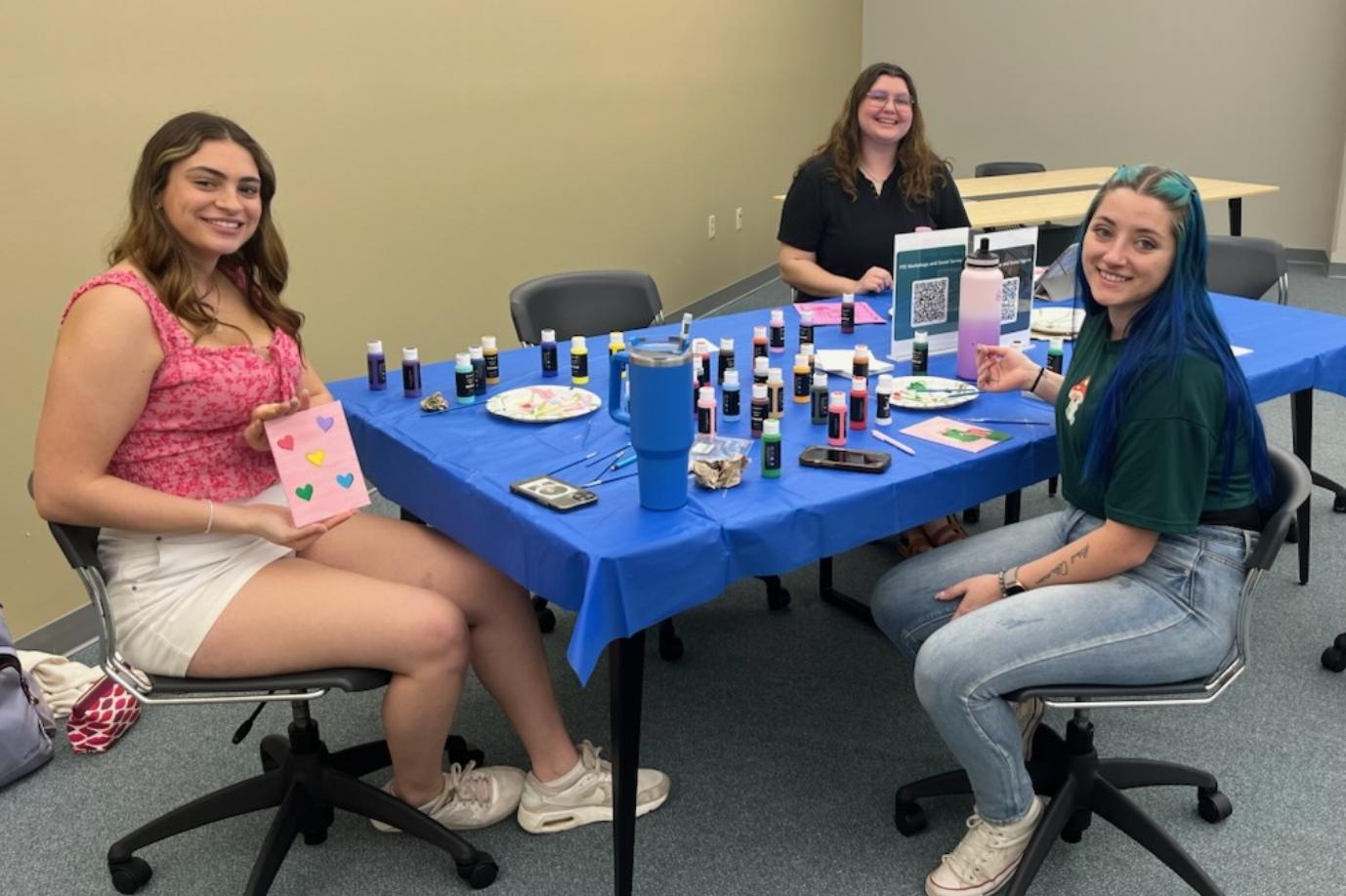 Three girls are smiling while at a table painting during a First Year Experience event