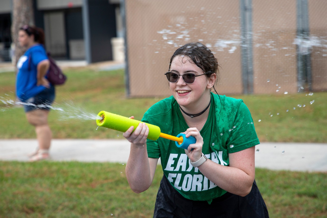 A female student uses a water gun while competing outside with other students.