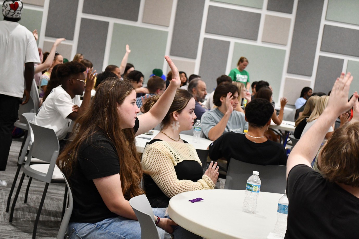 Students in the conference room raise their hands in answer to a question.