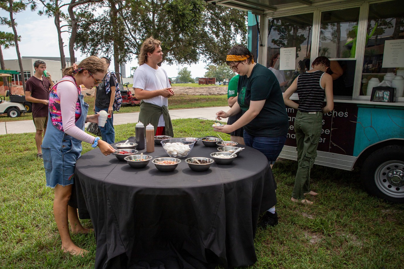 Students gather around an outdoor table near a food truck where lunch is being served.