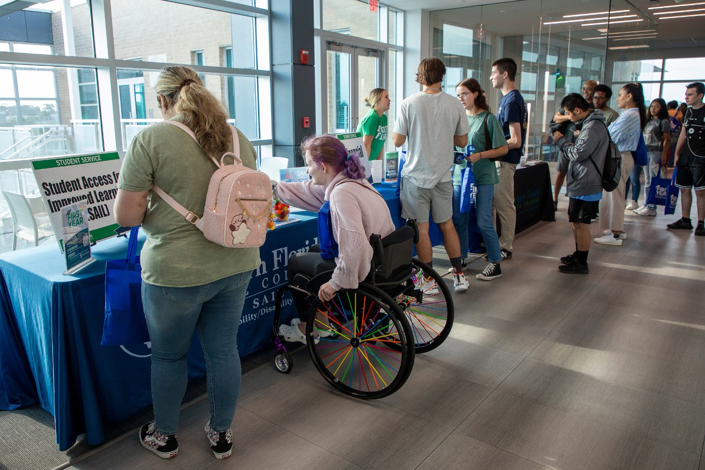 Students line the halls on the second floor of the Student Union. One student using a wheelchair is visiting the SAIL office table.