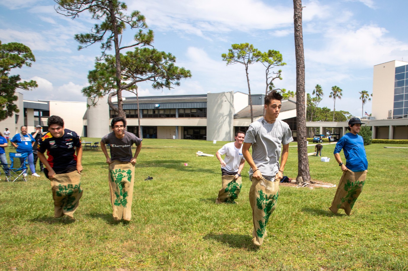 A group of diverse male students compete in a potato sack race.